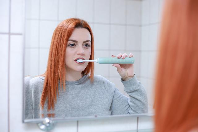 Kobieta myje zęby szczoteczką soniczna w łazience przed lustrem