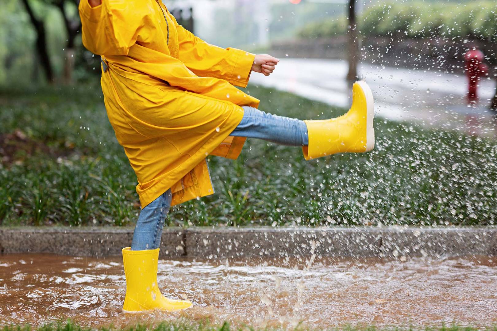 Dziewczyna podczas deszczu ma na sobie żółte kalosze i płaszcz przeciwdeszczowy